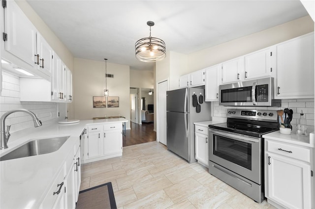 kitchen with a peninsula, stainless steel appliances, light countertops, white cabinetry, and a sink