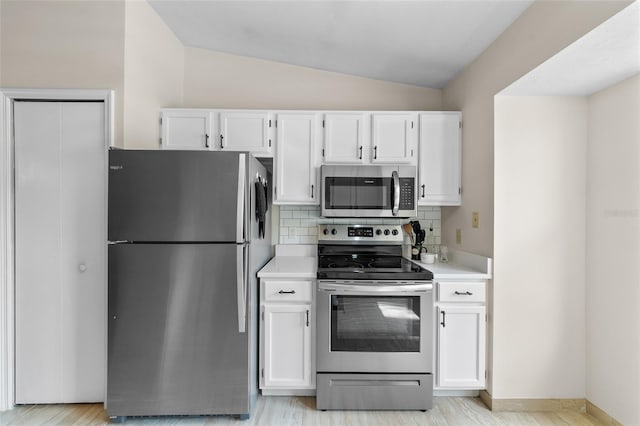 kitchen with vaulted ceiling, light countertops, appliances with stainless steel finishes, and white cabinetry