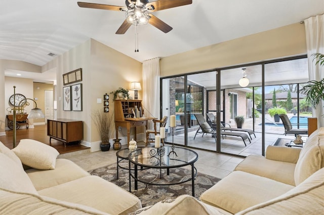 tiled living area with a ceiling fan, visible vents, vaulted ceiling, and baseboards