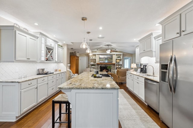 kitchen with a warm lit fireplace, appliances with stainless steel finishes, open floor plan, vaulted ceiling, and a sink