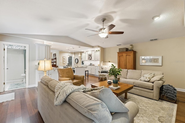 living room featuring a ceiling fan, visible vents, vaulted ceiling, and wood finished floors