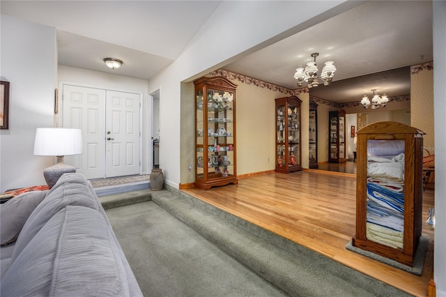 living area featuring wallpapered walls, a notable chandelier, baseboards, and wood finished floors