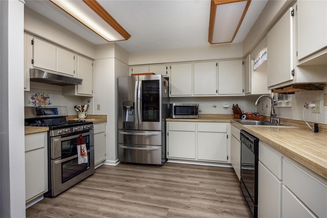 kitchen with under cabinet range hood, a sink, appliances with stainless steel finishes, light wood-type flooring, and tasteful backsplash