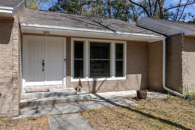 doorway to property featuring brick siding and roof with shingles