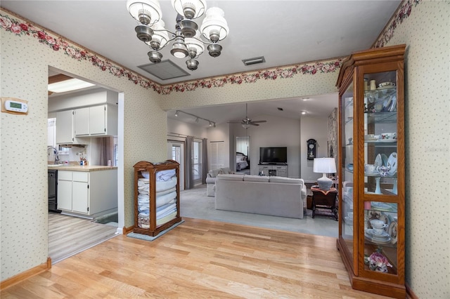 living area featuring light wood-style flooring, ceiling fan with notable chandelier, visible vents, rail lighting, and wallpapered walls