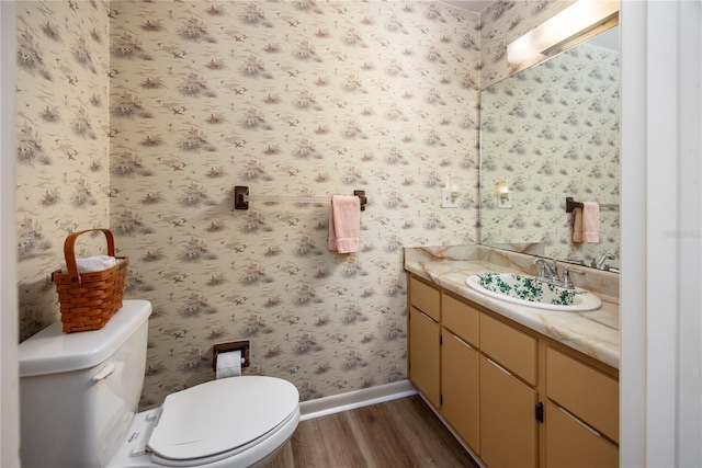 bathroom with wallpapered walls, baseboards, toilet, wood finished floors, and vanity