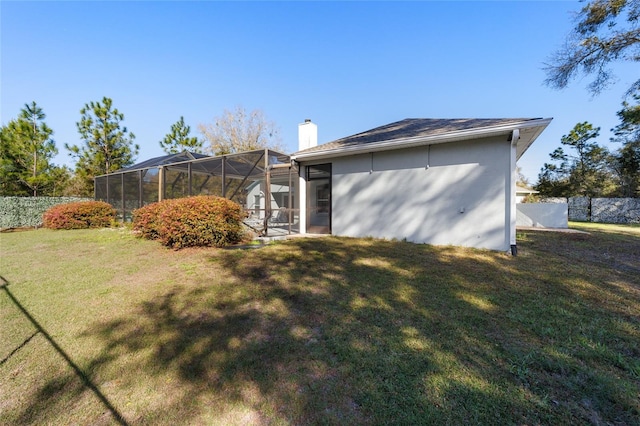 rear view of house featuring a yard, a chimney, a lanai, and fence