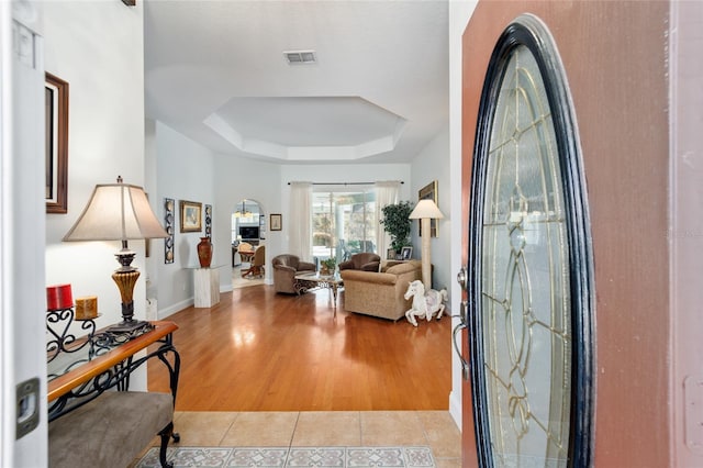 foyer entrance with light wood-type flooring, a tray ceiling, visible vents, and baseboards