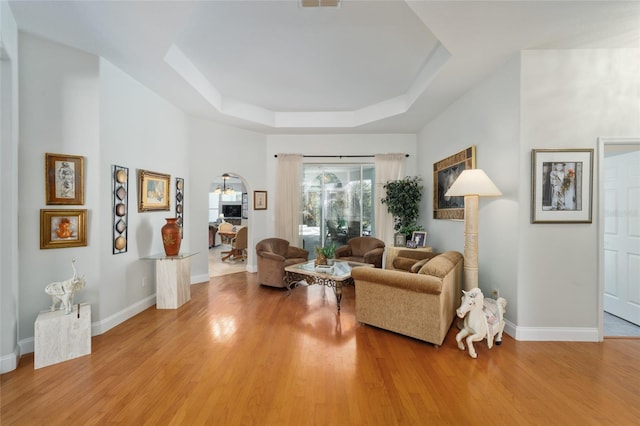 sitting room featuring light wood finished floors, a tray ceiling, and baseboards