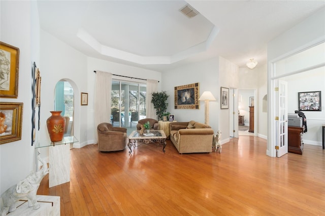 living area with visible vents, arched walkways, baseboards, a tray ceiling, and light wood-style floors