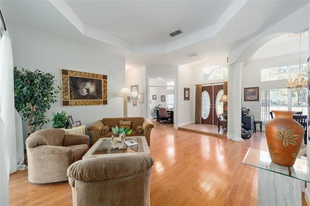 living area with a notable chandelier, a raised ceiling, visible vents, light wood-style floors, and ornate columns