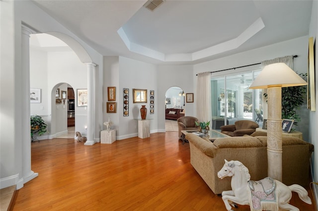 living area with arched walkways, a raised ceiling, visible vents, light wood-style flooring, and baseboards