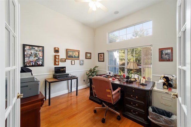 office area with ceiling fan, a high ceiling, light wood-style flooring, and baseboards