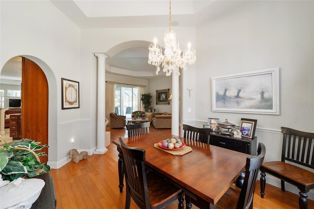 dining area with light wood-type flooring, baseboards, arched walkways, and a raised ceiling