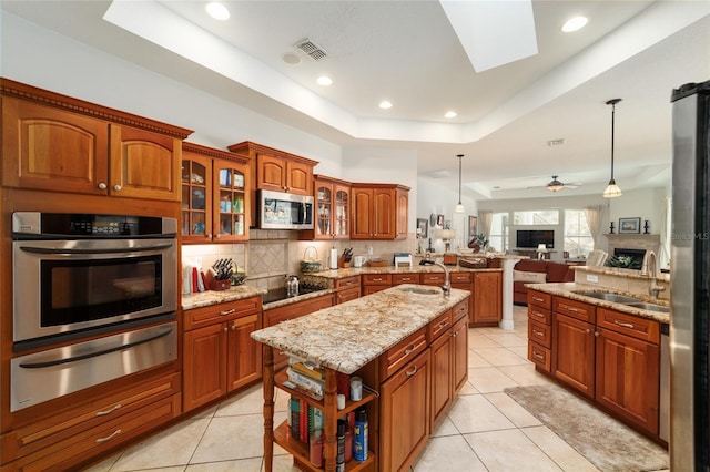 kitchen featuring a peninsula, a sink, appliances with stainless steel finishes, a warming drawer, and a tray ceiling