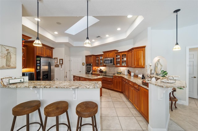 kitchen featuring a tray ceiling, stainless steel appliances, backsplash, glass insert cabinets, and a peninsula