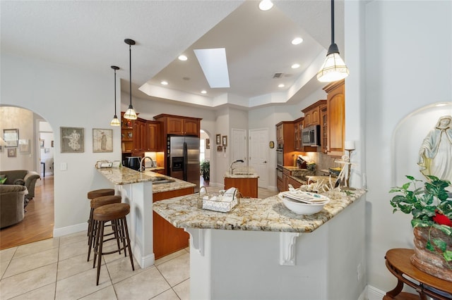 kitchen featuring arched walkways, stainless steel appliances, a peninsula, a breakfast bar, and a tray ceiling