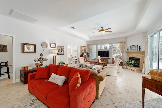 living room with a ceiling fan, a tray ceiling, a fireplace with raised hearth, and visible vents