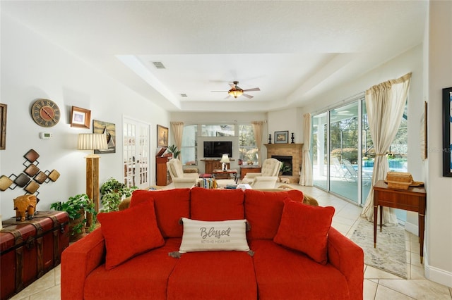 living room with a tray ceiling, a fireplace, light tile patterned floors, visible vents, and a ceiling fan