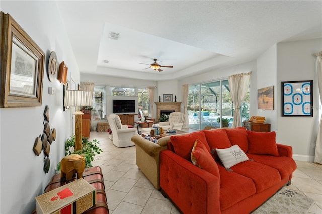 living room with a tray ceiling, a fireplace, visible vents, a ceiling fan, and light tile patterned flooring