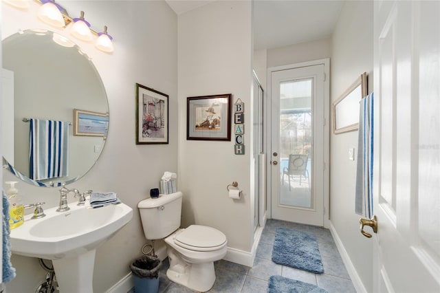 bathroom with toilet, a stall shower, a sink, tile patterned flooring, and baseboards