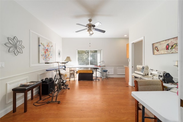 interior space featuring ceiling fan, wainscoting, light wood-type flooring, and a decorative wall