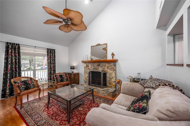 living area with high vaulted ceiling, a stone fireplace, wood finished floors, and a ceiling fan