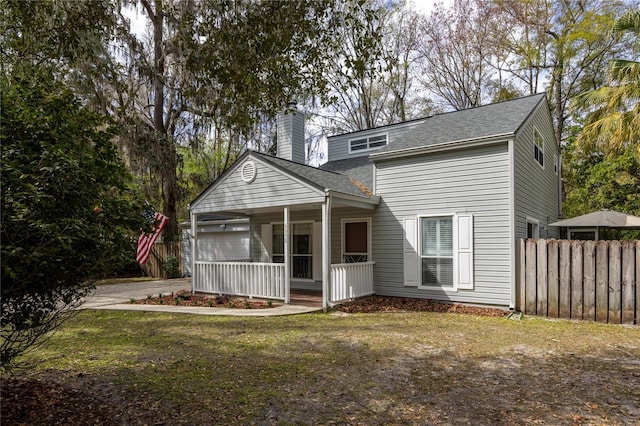 back of property with covered porch, a chimney, and fence