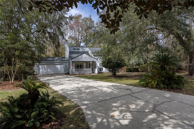 view of front of house with concrete driveway, a chimney, a porch, an attached garage, and a front lawn