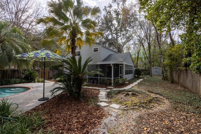 back of property with a patio, a fenced backyard, an outdoor structure, a sunroom, and a shed