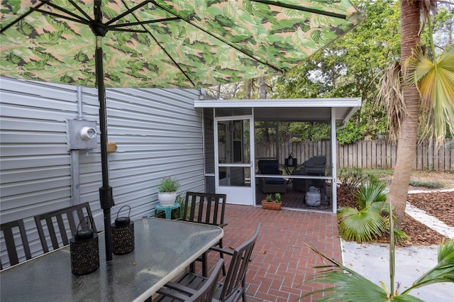 view of patio featuring outdoor dining space, fence, and a sunroom