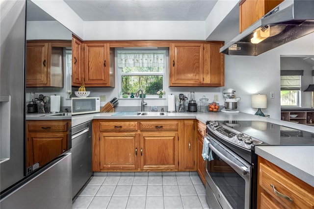 kitchen with brown cabinets, light countertops, appliances with stainless steel finishes, a sink, and under cabinet range hood