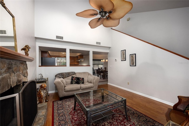 living room with visible vents, a stone fireplace, baseboards, and wood finished floors