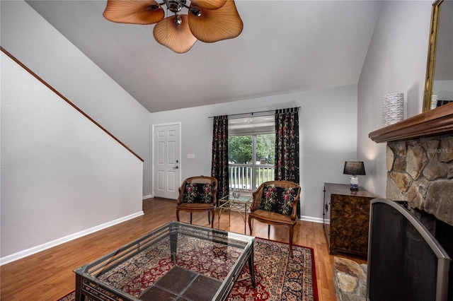 living area featuring lofted ceiling, a stone fireplace, wood finished floors, and baseboards