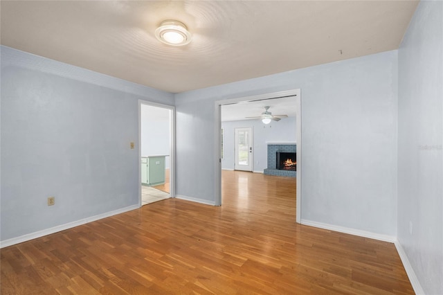 unfurnished room with a brick fireplace, light wood-style flooring, baseboards, and ceiling fan