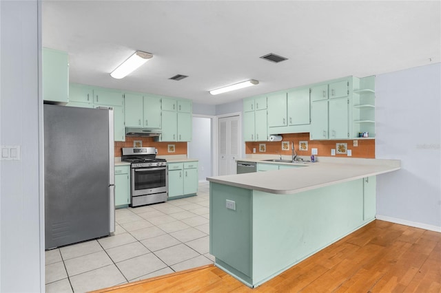 kitchen featuring under cabinet range hood, stainless steel appliances, a peninsula, visible vents, and light countertops