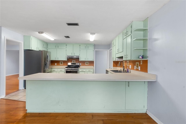 kitchen featuring visible vents, appliances with stainless steel finishes, a peninsula, green cabinets, and a sink