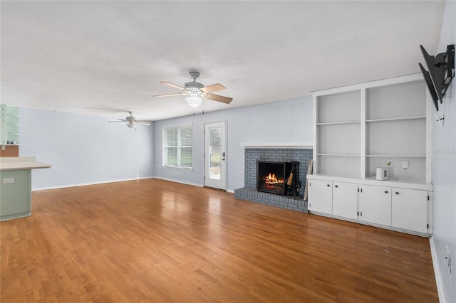 unfurnished living room with baseboards, ceiling fan, a brick fireplace, and light wood-style floors