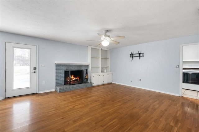 unfurnished living room with a brick fireplace, ceiling fan, baseboards, and wood finished floors