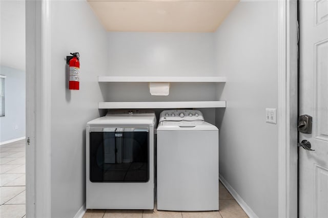 clothes washing area featuring light tile patterned floors, washing machine and clothes dryer, and baseboards