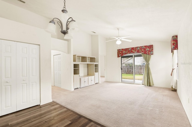 unfurnished living room featuring high vaulted ceiling, ceiling fan with notable chandelier, carpet floors, wood finished floors, and baseboards