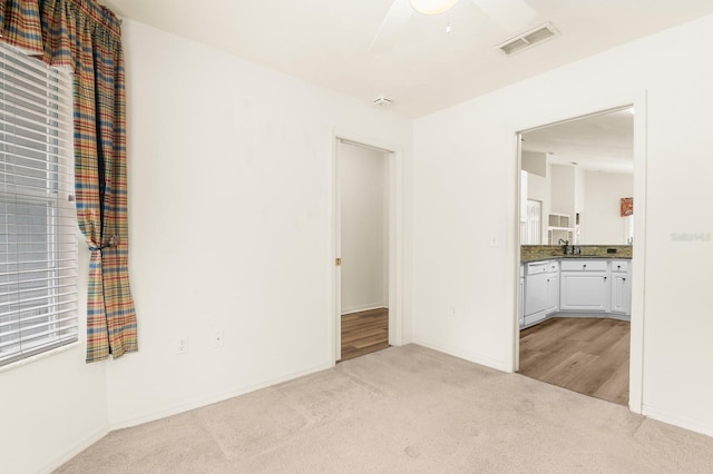 unfurnished room with ceiling fan, visible vents, a sink, and light colored carpet