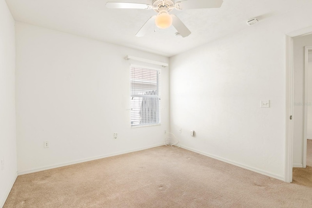 spare room with a ceiling fan, light carpet, and baseboards