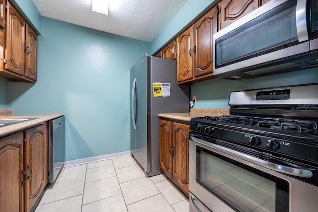 kitchen with brown cabinets, stainless steel appliances, light countertops, light tile patterned flooring, and baseboards