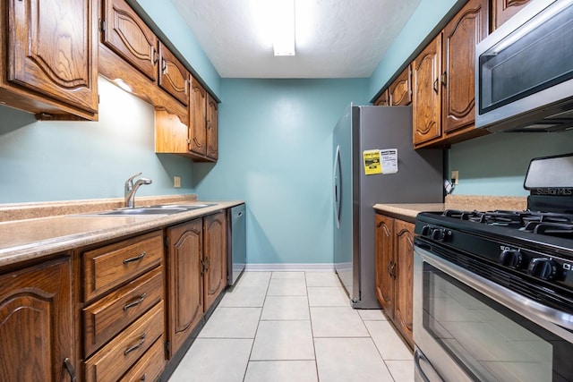 kitchen with light tile patterned floors, baseboards, appliances with stainless steel finishes, light countertops, and a sink