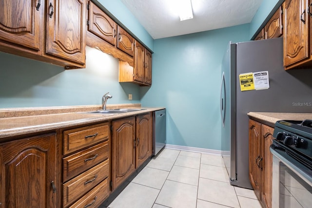 kitchen with stainless steel appliances, brown cabinetry, light tile patterned flooring, and a sink