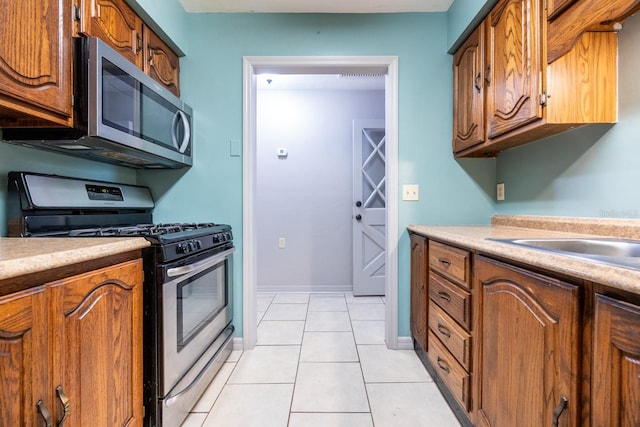 kitchen featuring brown cabinets, light tile patterned floors, light countertops, appliances with stainless steel finishes, and baseboards