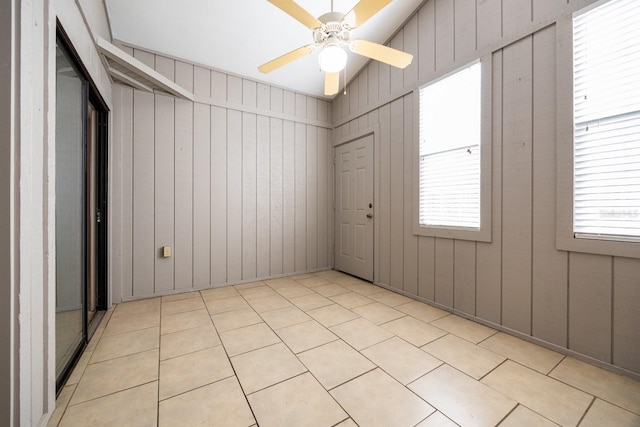 unfurnished room with light tile patterned floors, vaulted ceiling, a ceiling fan, and wooden walls