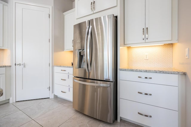 kitchen with backsplash, light tile patterned floors, light stone counters, white cabinets, and stainless steel fridge