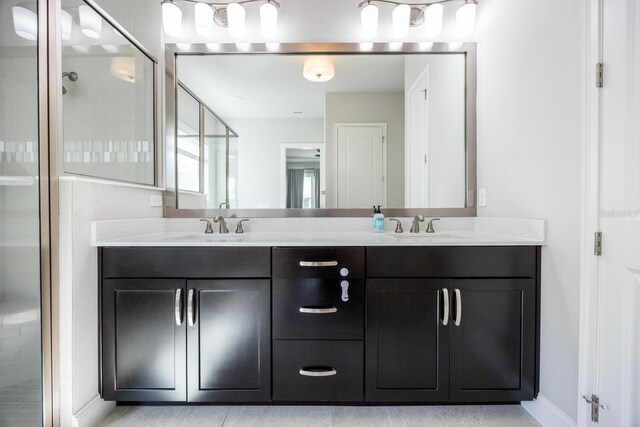 full bath with double vanity, a stall shower, baseboards, and a sink